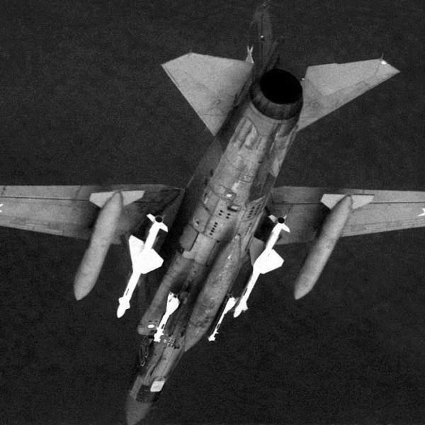 An air-to-air underside view of a Soviet MiG-23 Flogger aircraft. The aircraft is armed with AA-7 Apex missiles on wing pylons and AA-8 Aphid missiles on fuselage stations.